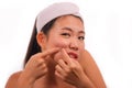 Young beautiful angry and upset Asian Korean woman with acne pooping head of pimple with her fingers on the mirror cleansing the Royalty Free Stock Photo