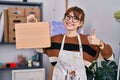 Young beautiful artist woman holding wooden case smiling happy and positive, thumb up doing excellent and approval sign Royalty Free Stock Photo