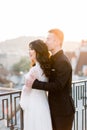 Young beautiful Asian bride and groom on the wedding walk, standing on the terrace of building, man embracing woman from Royalty Free Stock Photo