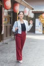 Young beautiful Asian business woman wear white suit and red pants smiling confidently,carry bag while walking in the city on a Royalty Free Stock Photo