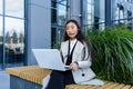 Young beautiful Asian business woman working in the air on a laptop, uses a headset for a video call, sitting near a office Royalty Free Stock Photo