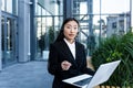 Young beautiful Asian business woman working in the air on a laptop, uses a headset for a video call, sitting near a office Royalty Free Stock Photo