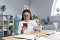 Young beautiful Asian businesswoman working in office, smiling and happy with victory, using phone, reading good news Royalty Free Stock Photo