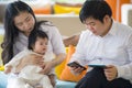 Young beautiful Asian Chinese family sitting at modern resort with workaholic man working business online with digital tablet and