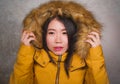 Young beautiful Asian Chinese woman feeling cold and chilly freezing feeling cold in Winter weather wearing yellow jacket with fur Royalty Free Stock Photo