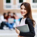 Young and beautiful Asian college student girls holding books, pose to camera with group of friends blur in background against Royalty Free Stock Photo