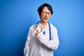 Young beautiful asian doctor girl wearing stethoscope and coat with blue cancer ribbon cheerful with a smile of face pointing with Royalty Free Stock Photo