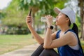 Young beautiful asian drinking water from bottle and using smartphone, she resting after jogging at green park Royalty Free Stock Photo