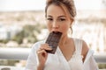 Young beautiful Asian girl in beige lace shorts,white shirt eating a chocolate bar on the balcony. selective focus. small focus Royalty Free Stock Photo