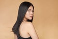 A young beautiful asian girl dressed in a black dress with natural makeup and shiny hair in the wind stands on a beige Royalty Free Stock Photo