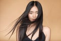 A young beautiful asian girl dressed in a black dress with natural makeup and shiny hair in the wind stands on a beige Royalty Free Stock Photo