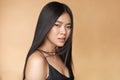 A young beautiful asian girl dressed in a black dress with natural makeup and shiny hair in the wind stands on a beige Royalty Free Stock Photo