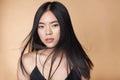 A young beautiful asian girl dressed in a black dress with natural makeup and shiny hair in the wind stands on a beige Royalty Free Stock Photo