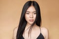 A young beautiful asian girl dressed in a black dress with natural makeup and shiny hair in the wind stands on a beige Royalty Free Stock Photo