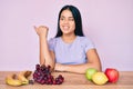 Young beautiful asian girl eating fresh and healthy fruit pointing thumb up to the side smiling happy with open mouth Royalty Free Stock Photo