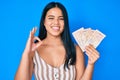 Young beautiful asian girl holding united kingdom pounds doing ok sign with fingers, smiling friendly gesturing excellent symbol