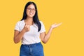 Young beautiful asian girl wearing casual clothes and glasses showing palm hand and doing ok gesture with thumbs up, smiling happy Royalty Free Stock Photo