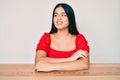 Young beautiful asian girl wearing casual clothes sitting on the table looking away to side with smile on face, natural expression Royalty Free Stock Photo