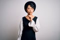 Young beautiful asian girl wearing casual dress and hat standing over isolated white background asking to be quiet with finger on Royalty Free Stock Photo