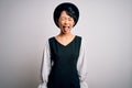 Young beautiful asian girl wearing casual dress and hat standing over isolated white background sticking tongue out happy with Royalty Free Stock Photo