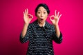 Young beautiful asian girl wearing casual jacket standing over isolated pink background looking surprised and shocked doing ok Royalty Free Stock Photo