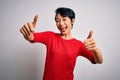 Young beautiful asian girl wearing casual red t-shirt standing over isolated white background approving doing positive gesture Royalty Free Stock Photo