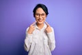 Young beautiful asian girl wearing casual shirt and glasses standing over purple background Smiling with open mouth, fingers Royalty Free Stock Photo