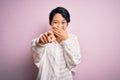 Young beautiful asian girl wearing casual shirt standing over isolated pink background laughing at you, pointing finger to the Royalty Free Stock Photo