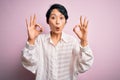 Young beautiful asian girl wearing casual shirt standing over isolated pink background looking surprised and shocked doing ok Royalty Free Stock Photo