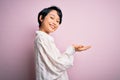 Young beautiful asian girl wearing casual shirt standing over isolated pink background pointing aside with hands open palms Royalty Free Stock Photo