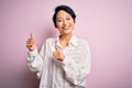 Young beautiful asian girl wearing casual shirt standing over isolated pink background Pointing to the back behind with hand and Royalty Free Stock Photo