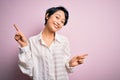 Young beautiful asian girl wearing casual shirt standing over isolated pink background smiling confident pointing with fingers to Royalty Free Stock Photo