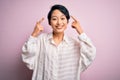 Young beautiful asian girl wearing casual shirt standing over isolated pink background smiling pointing to head with both hands Royalty Free Stock Photo
