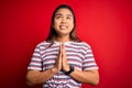 Young beautiful asian girl wearing casual striped t-shirt over isolated red background begging and praying with hands together Royalty Free Stock Photo