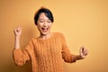 Young beautiful asian girl wearing casual sweater and diadem standing over yellow background Dancing happy and cheerful, smiling Royalty Free Stock Photo