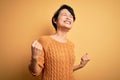 Young beautiful asian girl wearing casual sweater and diadem standing over yellow background very happy and excited doing winner Royalty Free Stock Photo