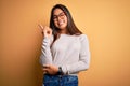 Young beautiful asian girl wearing casual sweater and glasses over yellow background with a big smile on face, pointing with hand Royalty Free Stock Photo