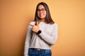 Young beautiful asian girl wearing casual sweater and glasses over yellow background cheerful with a smile of face pointing with Royalty Free Stock Photo