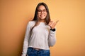 Young beautiful asian girl wearing casual sweater and glasses over yellow background smiling with happy face looking and pointing Royalty Free Stock Photo