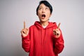 Young beautiful asian girl wearing casual sweatshirt with hoodie over white background amazed and surprised looking up and Royalty Free Stock Photo