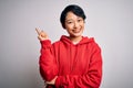 Young beautiful asian girl wearing casual sweatshirt with hoodie over white background with a big smile on face, pointing with Royalty Free Stock Photo