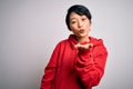 Young beautiful asian girl wearing casual sweatshirt with hoodie over white background looking at the camera blowing a kiss with Royalty Free Stock Photo