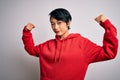 Young beautiful asian girl wearing casual sweatshirt with hoodie over white background showing arms muscles smiling proud Royalty Free Stock Photo