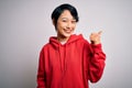 Young beautiful asian girl wearing casual sweatshirt with hoodie over white background smiling with happy face looking and Royalty Free Stock Photo