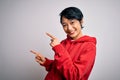 Young beautiful asian girl wearing casual sweatshirt with hoodie over white background smiling and looking at the camera pointing Royalty Free Stock Photo