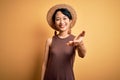 Young beautiful asian girl wearing casual t-shirt and hat over isolated yellow background smiling friendly offering handshake as Royalty Free Stock Photo