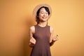 Young beautiful asian girl wearing casual t-shirt and hat over isolated yellow background very happy and excited doing winner Royalty Free Stock Photo