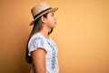 Young beautiful asian girl wearing casual t-shirt and hat standing over yellow background looking to side, relax profile pose with Royalty Free Stock Photo