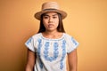 Young beautiful asian girl wearing casual t-shirt and hat standing over yellow background Relaxed with serious expression on face Royalty Free Stock Photo