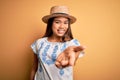 Young beautiful asian girl wearing casual t-shirt and hat standing over yellow background smiling cheerful offering palm hand Royalty Free Stock Photo